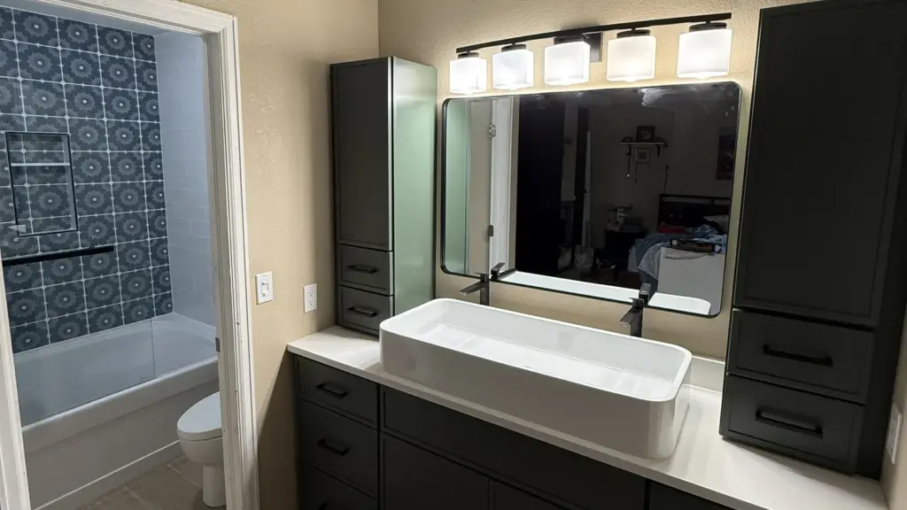 Remodeled bathroom with a dark vanity and linen towers, white trough sink, black fixtures, and blue patterned shower tile.