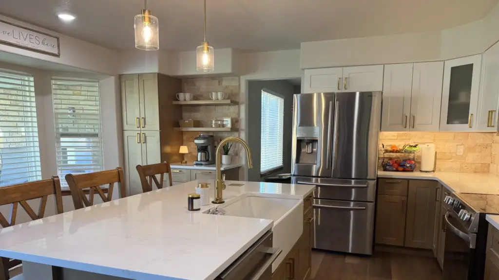 Remodeled kitchen with a white quartz island, farmhouse sink, brass faucet, two-tone cabinets, and stainless appliances.